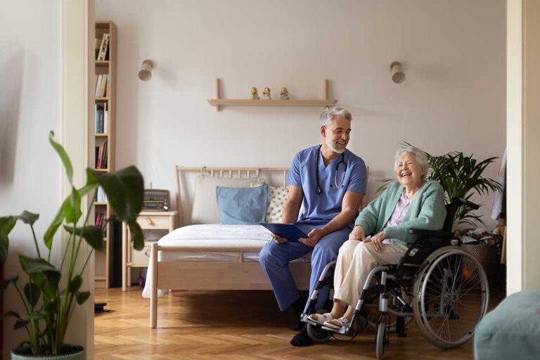 Seniors and caregivers sharing a conversation in a bright common room with seating and natural light.